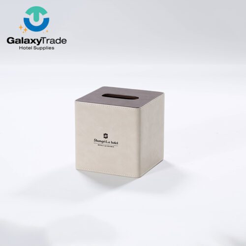 A Shangri-La branded luxury hotel square tissue box cover in beige faux leather with a dark wood-grain top.