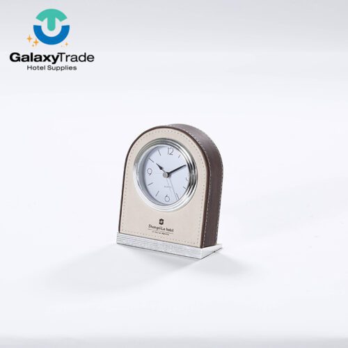A Shangri-La branded luxury hotel desk clock featuring a beige faux leather face, arch-shaped dark wood-grain body, and silver metallic base.