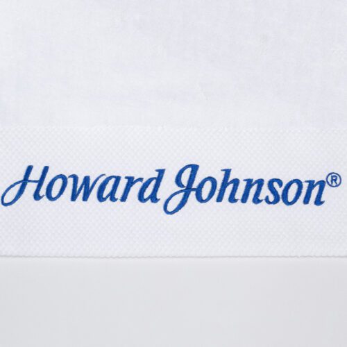 Close-up of a white cotton towel featuring the "Howard Johnson" brand name embroidered in blue on a textured white border.