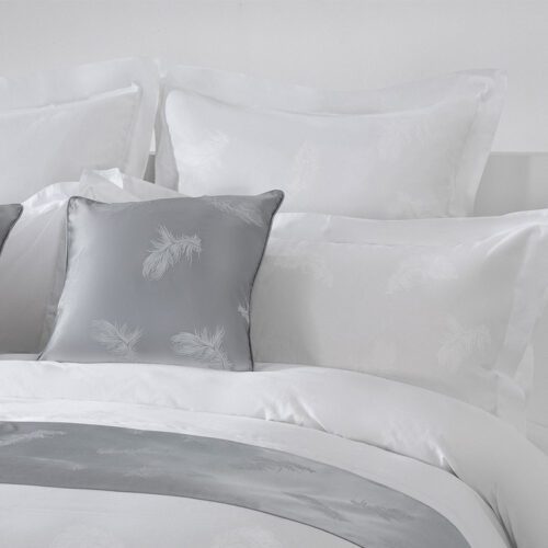 Luxury white hotel bedding featuring silver feather jacquard patterns with a matching grey bed runner and cushions.