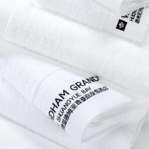 A close-up of a white plush cotton towel featuring the "Wyndham Grand" brand and "Huizhou Shuangyue Bay" hotel name embroidered in black.