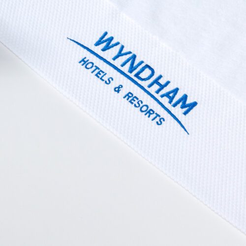 Close-up of a white cotton towel with "Wyndham Hotels & Resorts" embroidered in blue on a honeycomb border.