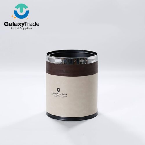A Shangri-La branded luxury hotel double-layer trash can in beige faux leather with a dark wood-grain trim and chrome top ring.
