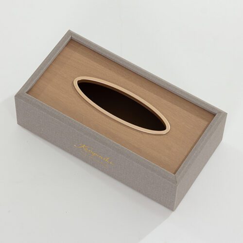 A Kempinski branded grey textured faux leather rectangular tissue box cover with a tan wood-grain top and a gold-trimmed oval dispensing hole.