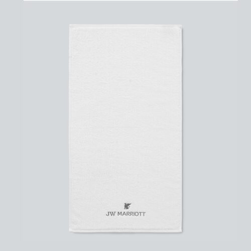 An official JW Marriott white plush cotton bath towel featuring the brand name and Griffin logo embroidered in charcoal grey at the bottom.