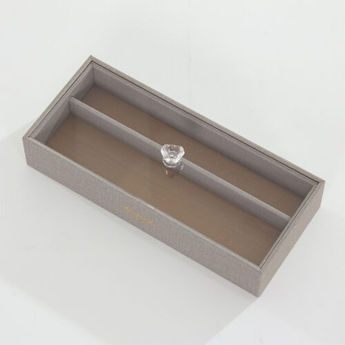 A Kempinski branded grey textured faux leather tea bag box with a clear acrylic lid and a crystal-style knob.