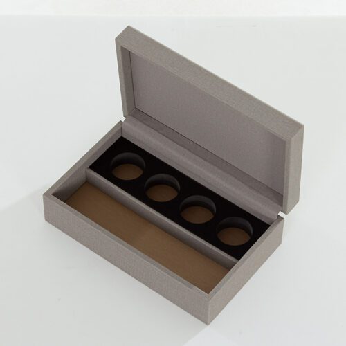 An open Kempinski branded grey textured faux leather coffee capsule box showing a black 4-slot insert and a tan interior base.