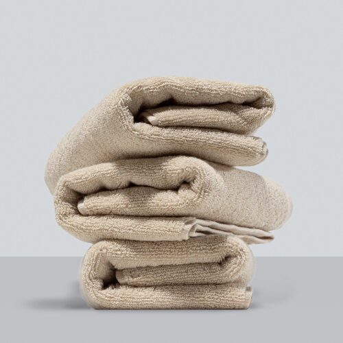 A stack of three neatly folded sand-beige plush cotton towels showcasing a dense and soft loop pile texture.
