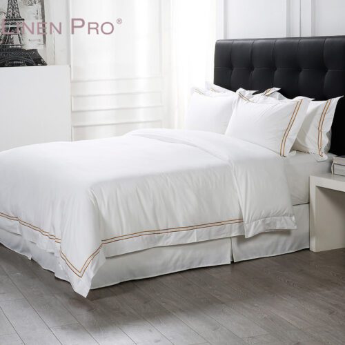 Luxury white hotel bedding set featuring a sharp gold double-line embroidered border on the duvet and stacked pillowcases.