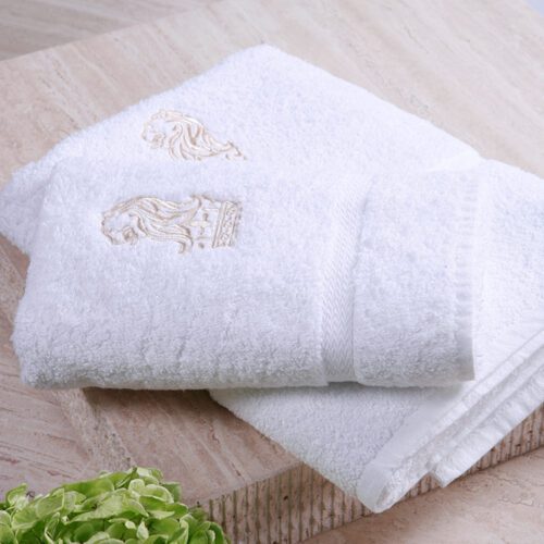 A set of folded luxury white plush cotton towels featuring detailed golden lion and crown embroidery.