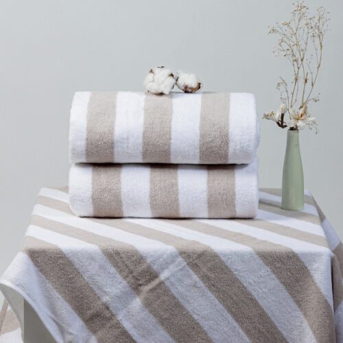 Two neatly rolled beige and white striped plush beach towels stacked on a matching striped surface with decorative cotton bolls and flowers.