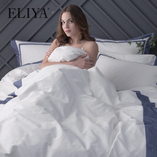 A high-end hotel bed featuring a crisp white duvet cover with a bold cobalt blue frame border and matching pillowcases.