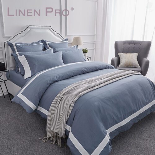 A modern luxury bed featuring a slate blue duvet cover with a crisp white frame border and matching Oxford pillowcases.