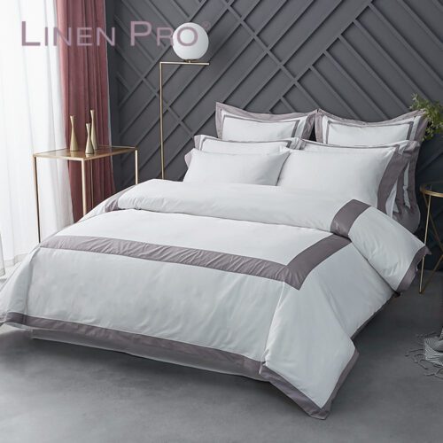 A premium white hotel bed with a duvet cover featuring a wide mauve purple border and matching pillowcases.