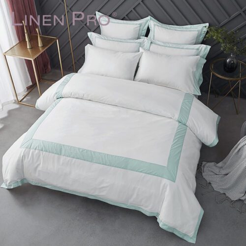 A high-end white hotel bed with a duvet cover featuring a bold midnight blue border and matching pillows.