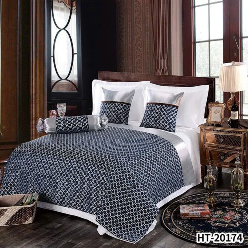 A modern hotel bed with white linens featuring a navy bedspread with silver geometric circle patterns and matching pillowcases.