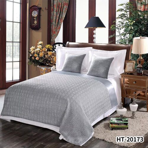 A minimalist hotel bed with silver-grey bedding featuring a geometric square jacquard pattern and a matching satin border.