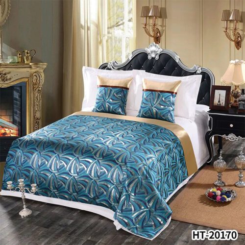 A modern hotel bed with a teal bedspread featuring silver arched geometric patterns and a wide gold satin border.