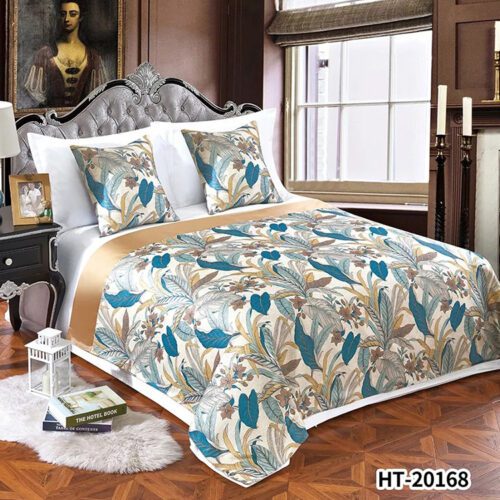 A luxury hotel bed with white linens featuring a golden-cream bedspread with vibrant teal and blue leaf patterns and wide gold satin borders.