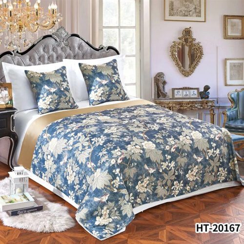 A luxury hotel bed with white linens featuring a blue bedspread with white floral and bird patterns and a gold satin border.