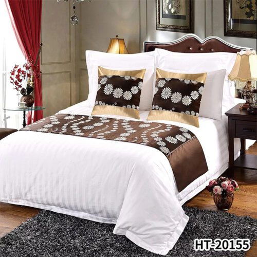 A luxury hotel bed with white striped linens featuring a coffee brown bed runner with white daisy jacquard and gold satin borders.