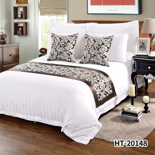A classic hotel bed with white linens featuring a coffee brown and silver scroll patterned runner and matching pillows.