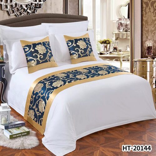 A luxury hotel bed with white striped linens featuring a navy blue and gold peony floral bed runner and matching pillows.