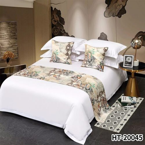 A luxury hotel bed with white linens featuring a vintage map and floral patterned runner and matching pillows.