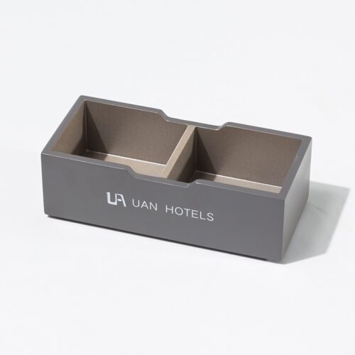 A professional product shot of a UAN HOTELS branded matte grey lacquered organizer with two champagne gold compartments.