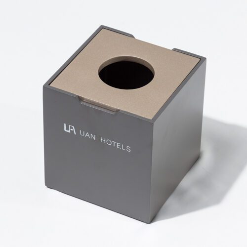A professional product shot of a UAN HOTELS branded matte grey square tissue box with a champagne gold top opening.