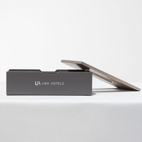 A professional side-angle view of a UAN HOTELS branded matte grey lacquered rectangular tissue box with the lid partially open.