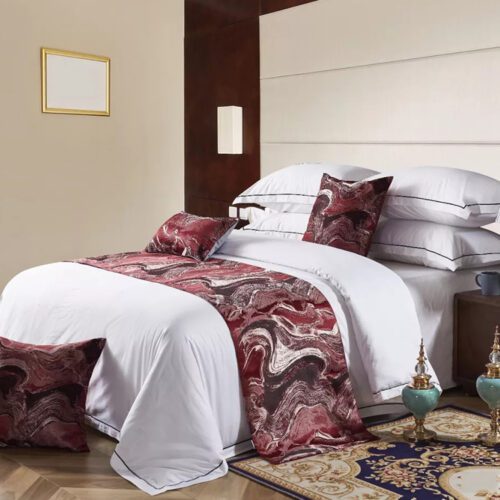 A luxury hotel bed with white linens featuring a burgundy marble texture bedspread and matching pillows.