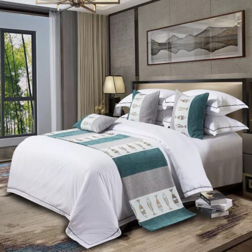 A modern hotel bed with white linens featuring a beige and slate grey color-block bedspread and matching pillows.