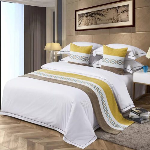 A modern hotel bed with white linens featuring an ochre yellow and grey color-block bedspread and matching pillows.