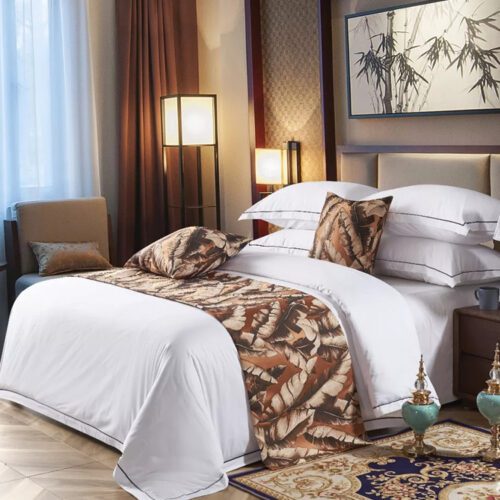 A luxury hotel bed with white linens featuring a vintage brown bedspread with a banana leaf pattern and matching pillows.