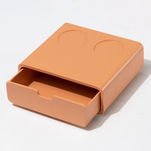 A professional product shot of a vibrant orange lacquered hotel coffee organizer featuring a pulled-out storage drawer and two circular top indentations.