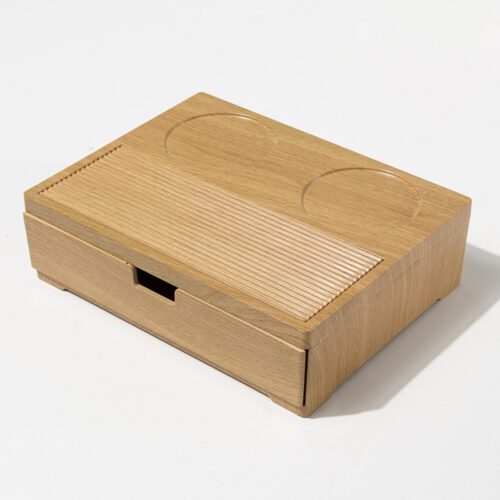 A professional product shot of a Banyan Tree branded natural wood hotel tea and coffee station with a storage drawer and cup grooves.