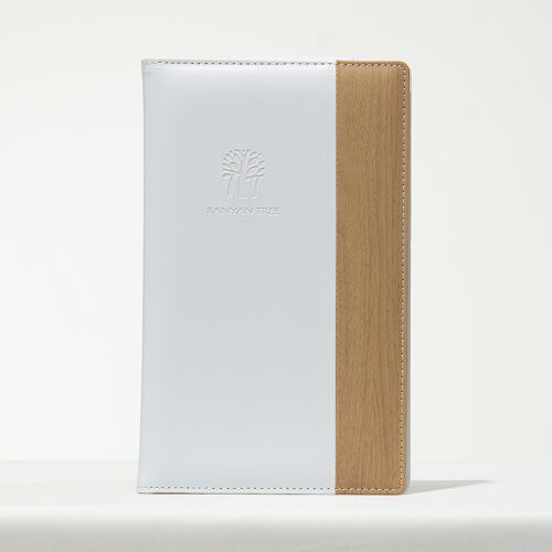 A professional product shot of a Banyan Tree branded dual-material folder featuring white leather and a wood-textured vertical accent.