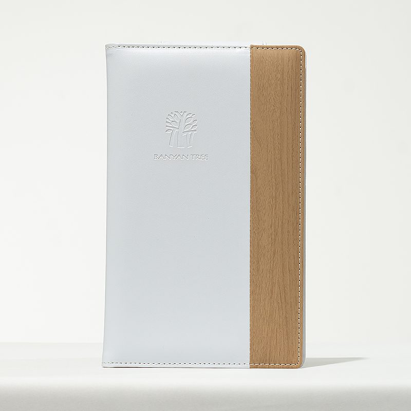 A professional product shot of a Banyan Tree branded dual-material folder featuring white leather and a wood-textured vertical accent.
