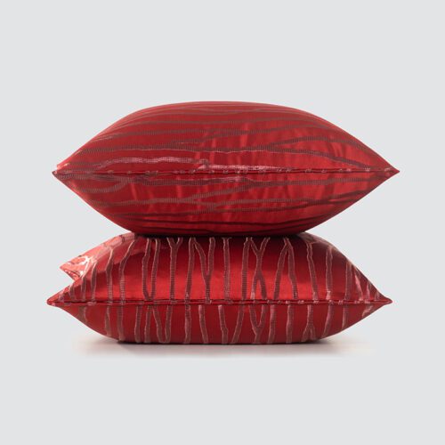 A stack of two luxury crimson red satin pillows featuring a high-gloss finish and horizontal linear embroidery.