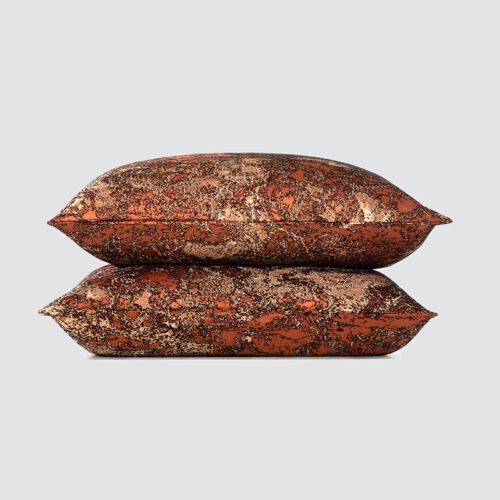 A stack of two luxury copper and charcoal throw pillows with a distressed metallic abstract pattern and high-gloss finish.