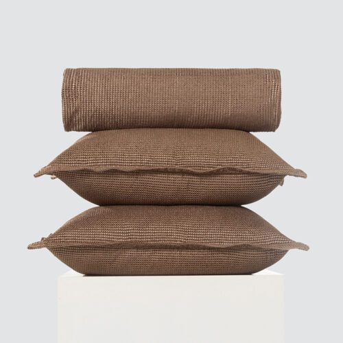 A stack of two coffee brown waffle weave pillows and a matching rolled bed runner with decorative frayed edges.