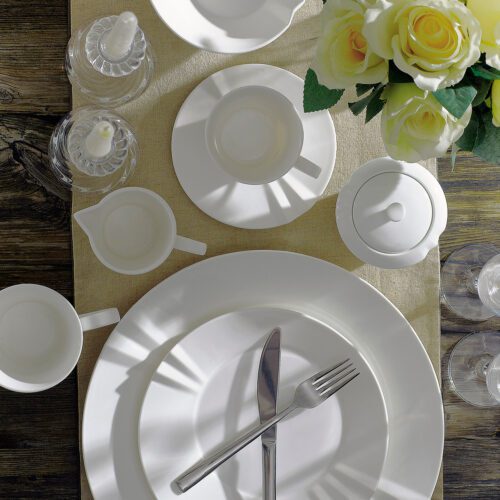 A top-down view of a luxury white porcelain dinnerware set featuring scalloped edges on plates, bowls, and coffee service items.