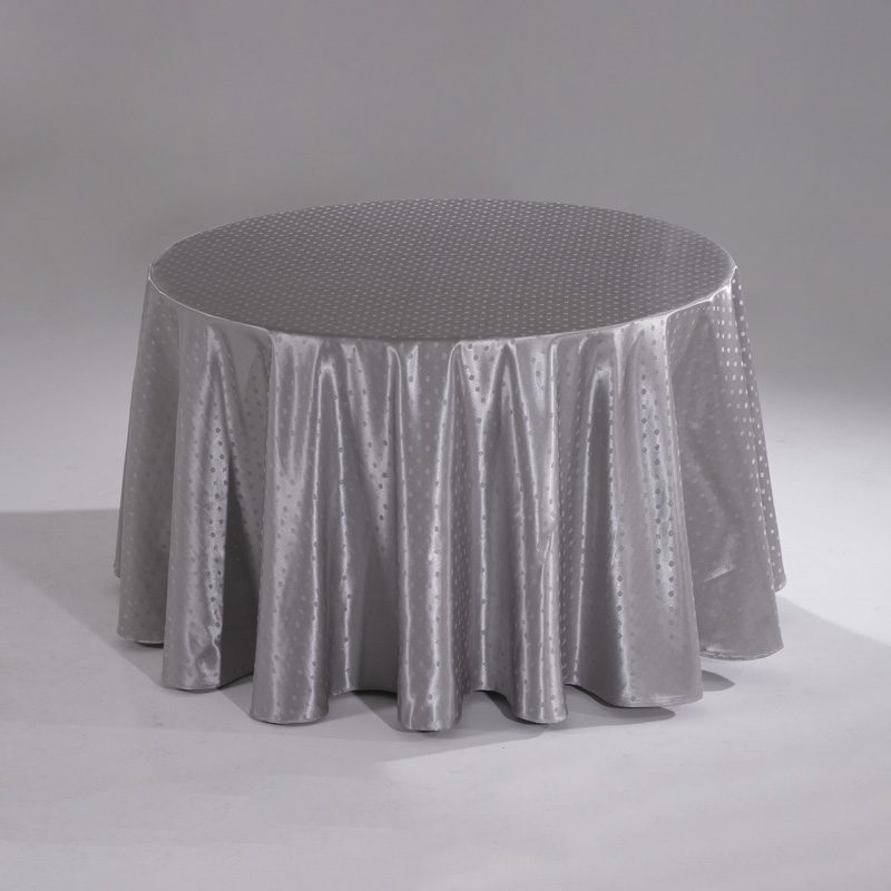 A large silver round polyester tablecloth with an intricate snowflake jacquard pattern draped over a banquet table.