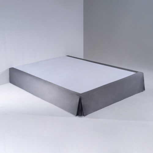 A tailored charcoal grey bed skirt with a single corner pleat fitted onto a white mattress base.