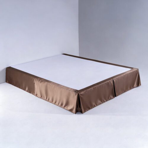 A luxurious bronze satin bed skirt with a silky sheen and tailored corner pleats on a hotel mattress base.