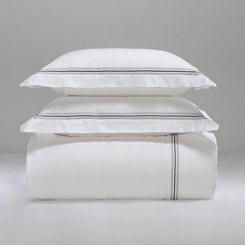 A stack of luxury white hotel pillows and a duvet featuring black embroidered linear detailing.