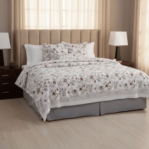 A luxury boutique hotel bed featuring a white bedding set with a detailed red and green floral botanical print and a tailored grey bed skirt.