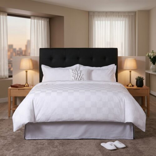 A luxury hotel bed featuring white linens with a tonal checkered jacquard pattern and a black tufted headboard in a modern suite.