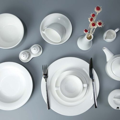 A comprehensive minimalist white porcelain dinnerware set featuring a subtle ribbed texture on plates, bowls, and a teapot.